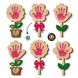 Pode incluir: Decorações de madeira em forma de flor com desenhos de impressões de mãos cor-de-rosa. Algumas flores têm folhas verdes e vasos castanhos com o texto "Happy Mother's Day". Outras flores têm laços cor-de-rosa. A imagem mostra 6 variantes.