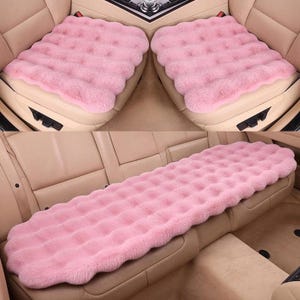 Puede incluir: Fundas de asiento de coche rosas. La imagen muestra dos fundas de asiento delanteras y una funda de asiento trasera. Las fundas están hechas de un material suave y afelpado con un borde ondulado. Las fundas son de color rosa liso.