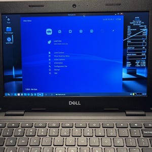 May include: A black Dell laptop displaying the RetroArch interface on its screen. The screen shows a blue background with various icons and text options. The keyboard is visible below the screen.