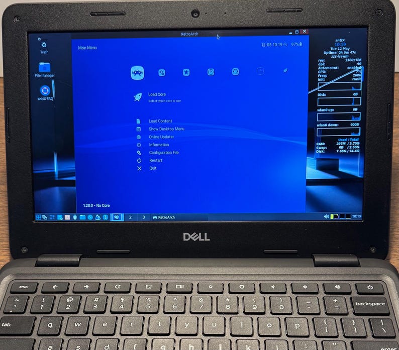 May include: A black Dell laptop displaying the RetroArch interface on its screen. The screen shows a blue background with various icons and text options. The keyboard is visible below the screen.