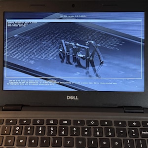 May include: A black Dell laptop displaying the GNU GRUB version 2.12-9-deb13u1 boot menu on its screen. The screen shows text options including antix 23 trixie, memory test, and UEFI firmware settings over a blue background with a logo.