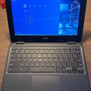 May include: A black Dell laptop with a dark gray keyboard and a large trackpad. The screen displays a blue interface with the text RetroArch, Main Menu, and system information including CPU, RAM, and disk usage statistics on the right side.