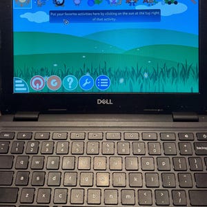 May include: A black Dell laptop displaying an educational program with cartoon characters and the text: "Put your favorite activities here by clicking on the sun at the top right of that activity."