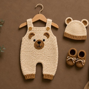 May include: A cream-colored crochet overall with a bear face design, featuring two brown buttons at the straps. The set includes a matching cream and brown bear-ear beanie and a pair of brown crochet booties with white laces, all displayed together.