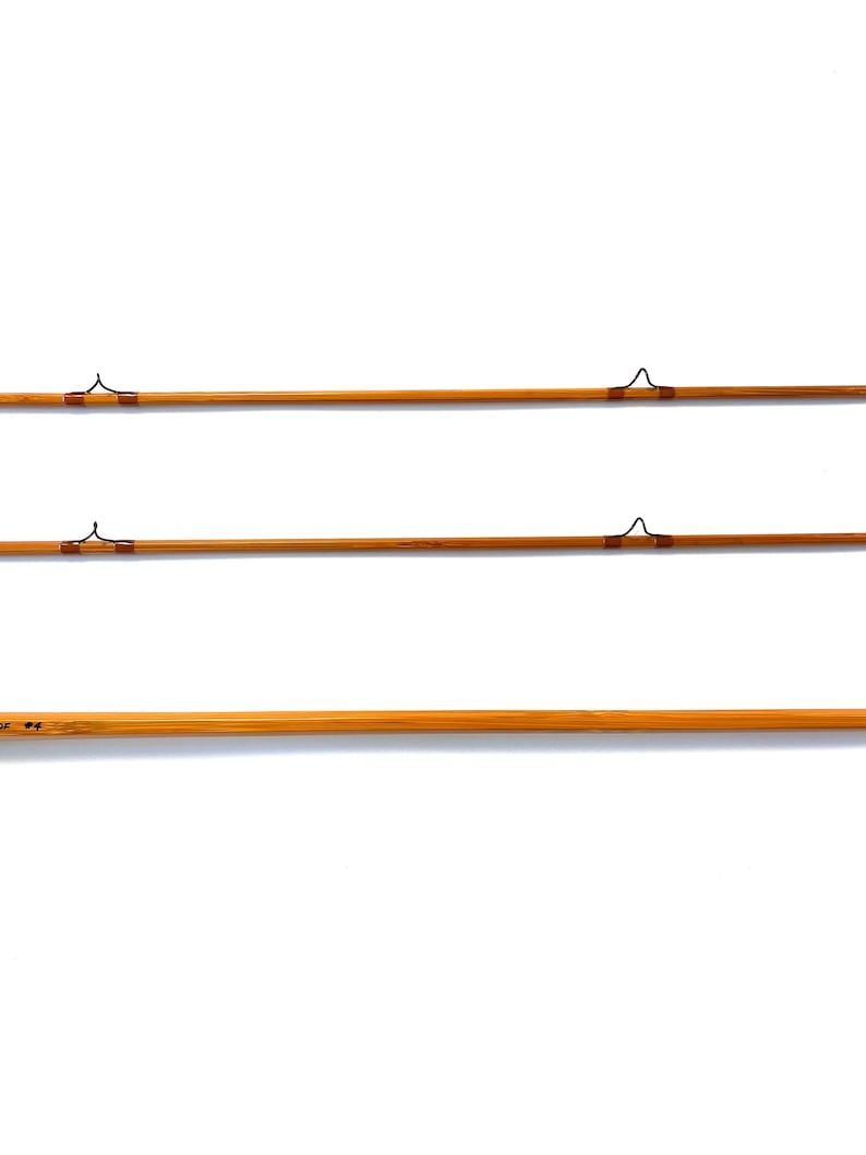 Peut inclure: Trois cannes &agrave; p&ecirc;che &agrave; la mouche vintage, de couleur marron clair avec des d&eacute;tails marron fonc&eacute;. Chaque canne pr&eacute;sente des guides en m&eacute;tal et un design classique, sur fond blanc. Les cannes fines semblent &ecirc;tre en bambou.