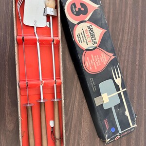 May include: A vintage 3-piece barbecue set in its original box. The set includes a fork, spatula, and basting brush with wooden handles and chrome-plated heads. The box is black with red and white accents and features the text "BARBECUE SET".