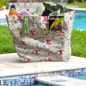 May include: A large tote bag with a floral and Elmo print, filled with items. The bag has green handles and a green tassel. A bottle of Banana Boat Sport sunscreen is visible. A Sesame Street tag is attached.