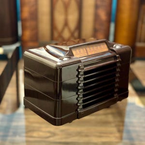 May include: A dark brown vintage radio with a glossy finish. The radio has a speaker grille, a tuning dial, and a rectangular shape. It's likely from the mid-20th century, a classic example of mid-century design, and would look great in any home.