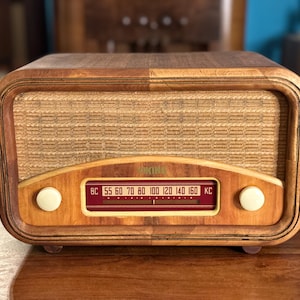 May include: A wooden radio with a rounded rectangular frame, featuring a textured beige fabric speaker grille, two white circular knobs, and a horizontal red dial display with the text VIKING and frequency markings from 55 to 160 KC.