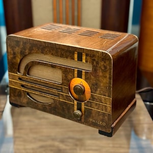 Può includere: Radio Philco vintage con mobile in legno. La radio presenta una finitura in legno scuro, un pannello frontale decorativo, un quadrante di sintonizzazione e il marchio "PHILCO". Il design della radio è classico e retrò.