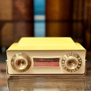 May include: A vintage yellow Westinghouse cordless transistor radio with a cream-coloured front panel, two circular gold-toned tuning knobs, and a central rectangular badge featuring the text Cordless Westinghouse Transistor in white lettering.