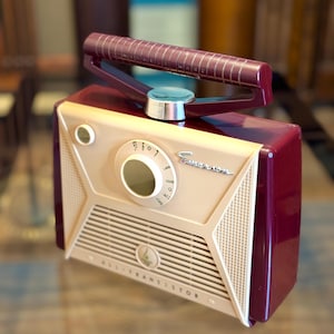 May include: A vintage-style radio in cream, burgundy, and beige. The radio features a dial, speaker grill, and a handle. The text "ALL TRANSISTOR" is visible on the front. The radio has a retro design.