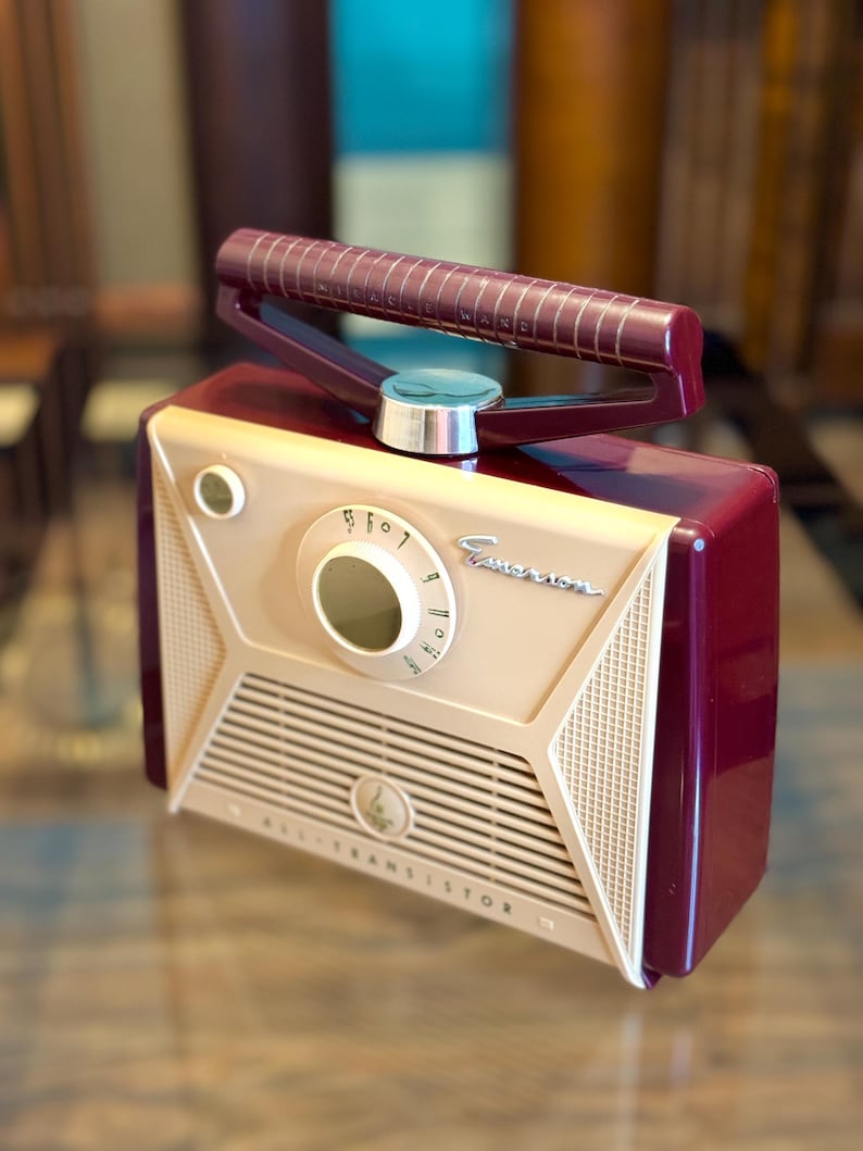 May include: A vintage-style radio in cream, burgundy, and beige. The radio features a dial, speaker grill, and a handle. The text "ALL TRANSISTOR" is visible on the front. The radio has a retro design.