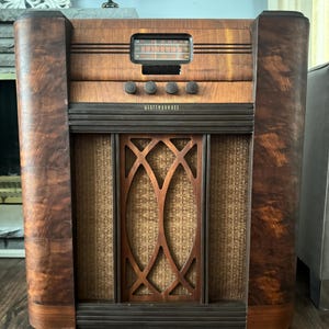 May include: A vintage Westinghouse radio in a wooden cabinet. The radio has a dark wood grain finish, a speaker grill with a decorative pattern, and a tuning dial. The text "WESTINGHOUSE" is visible on the front.