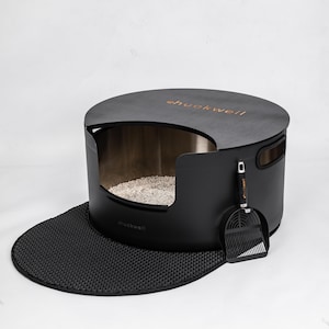 May include: A modern black cat litter box with a matching scoop and a textured mat. The litter box has a circular top with the brand name "huckwell" in a copper color. The interior is a light metallic color, and the mat is black.