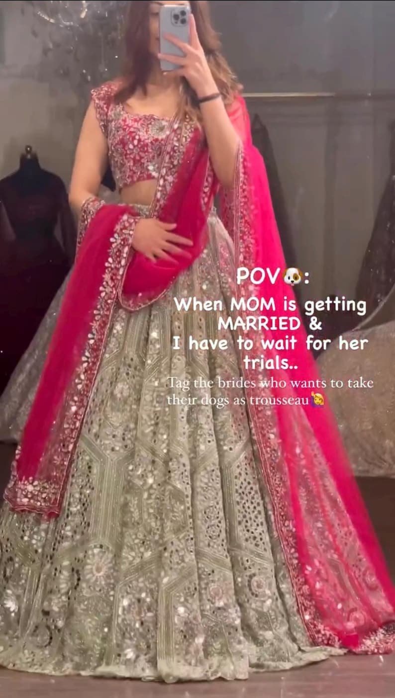 A person wearing a light green lehenga skirt with silver embroidery and mirrors, a dark red embroidered choli, and a hot pink net dupatta, with text overlaying the image.
