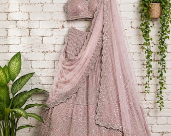Op de afbeelding: Een oudroze lehenga-set bestaande uit een mouwloze top en een volumineuze rok tot op de grond, beide rijkelijk versierd met ingewikkeld zilverkleurig borduurwerk en reflecterend spiegelwerk. Een bijpassende transparante dupatta met schulprand.