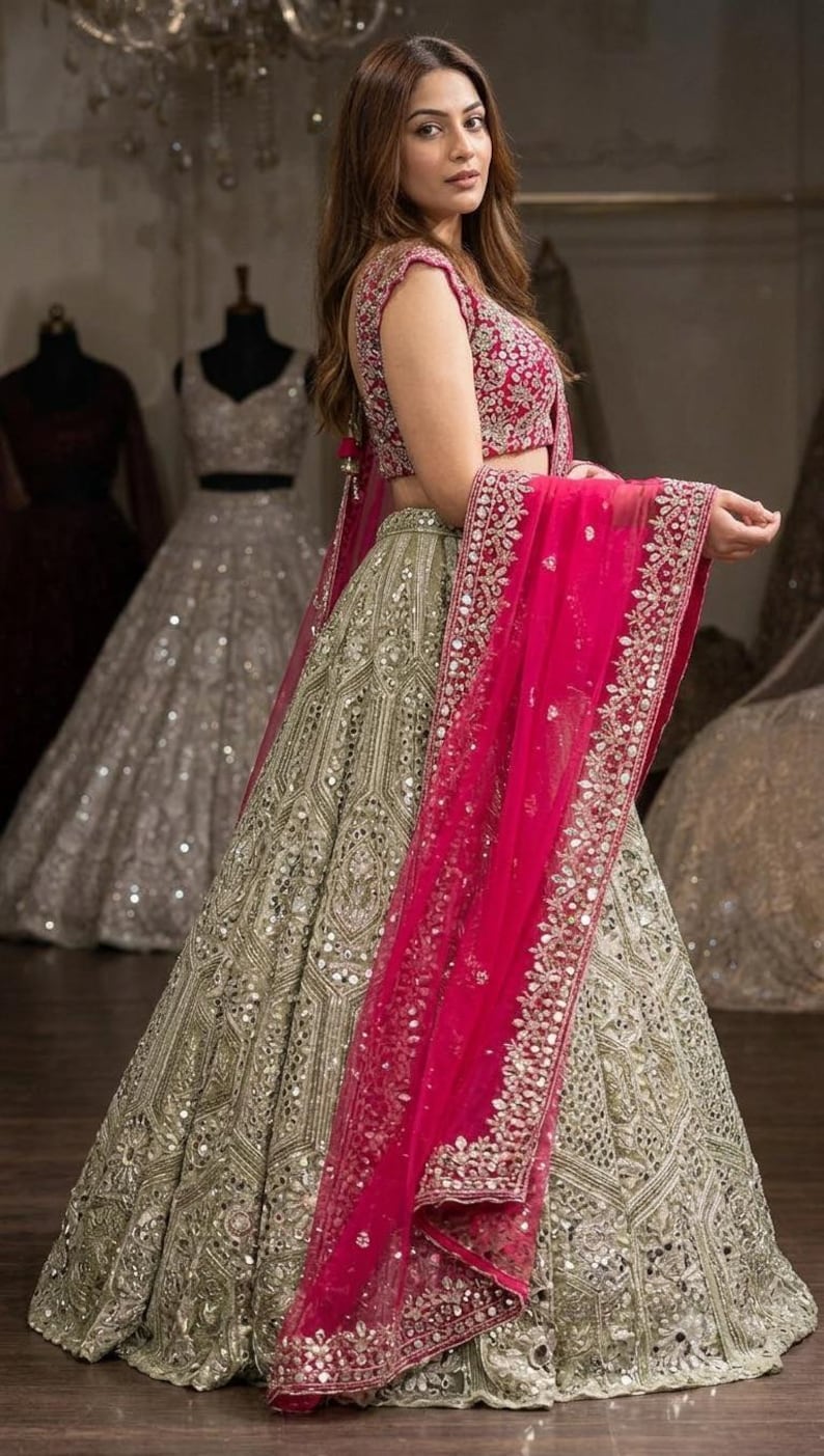 A person from the side, wearing a dark red embroidered choli, a light green lehenga skirt with silver embroidery and mirrors, and a hot pink net dupatta draped over their shoulder.
