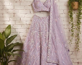 May include: A lavender lehenga set featuring a sleeveless V-neck blouse and a voluminous skirt, both adorned with intricate floral embroidery, sequins, and beadwork. A matching sheer lavender dupatta with a decorative border is draped over the side.