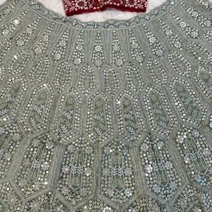 A flat lay of a dark red embroidered choli and a light green lehenga skirt with silver embroidery and mirrors, on a white textured surface.