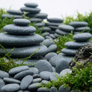 Puede incluir: Una imagen serena de piedras de río grises apiladas, algunas con gotas de agua, dispuestas en medio de musgo verde vibrante. Las piedras varían en tamaño, creando una estética equilibrada y natural. La escena evoca una sensación de tranquilidad.