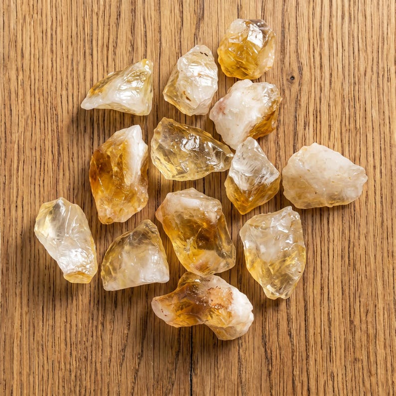 May include: A collection of raw citrine crystals, showcasing a range of golden yellow and translucent hues. The crystals are irregularly shaped and vary in size, resting on a light brown wooden surface.