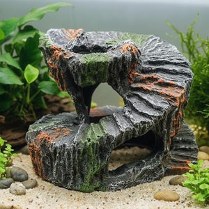 Può includere: Ornamento decorativo per acquario a forma di formazione rocciosa. La struttura grigia, nera e arancione presenta un design a spirale con un'apertura centrale. Dettagli verdi simili a muschio aggiungono dettagli alla roccia artificiale. Posizionato su una superficie sabbiosa.