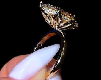 Könnte beinhalten: Ein goldener Ring mit einem großen, facettierten, gelben Edelstein. Der Ring hat ein dünnes, poliertes Band und die Fassung weist aufwendige Details mit kleineren Akzentsteinen auf. Der Ring ist vor einem schwarzen Hintergrund.