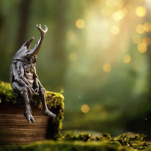 Puede incluir: Una escultura detallada de una criatura parecida a un escarabajo con grandes cuernos, sentada sobre una superficie de madera cubierta de musgo. La figura es de color gris oscuro, con detalles intrincados. El fondo es un bosque verde borroso con luz dorada suave.