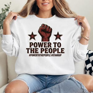 Whether worn casually, at gatherings, or as a conversation starting outfit, this shirt adds a bold statement to everyday style. The balanced combination of strong typography and symbolic imagery creates a graphic that is both eye-catching and meaningful.