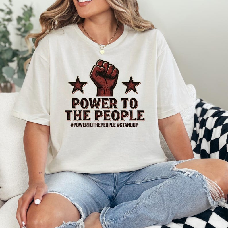 This Power To The People shirt features a bold raised fist graphic combined with strong typography that symbolizes unity, activism, and the voice of the people. Inspired by historic protest movements and modern social activism, the design captures the spirit of standing together and expressing collective strength. The clean layout keeps the message clear while maintaining a visually striking graphic style.