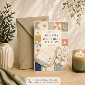 Puede incluir: Una tarjeta de felicitación rectangular con un diseño de colcha de retazos en colores suaves, con motivos de estrellas, corazones y soles. El texto dice "SO HAPPY YOU'RE HERE LITTLE ONE" sobre una ilustración de una manta y patucos de bebé.