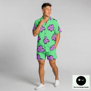 May include: A matching green short-sleeve shirt and shorts set with a large purple flower pattern. The shirt has a button-down front and a collar. The shorts have a matching floral design. The Fun Design Studio logo is in the bottom right corner.