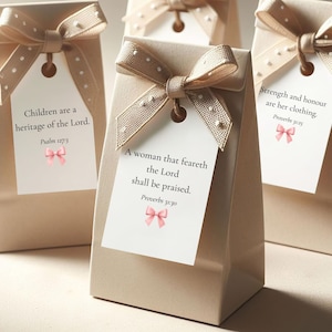 May include: Beige gift bags with polka dot ribbon bows and tags. Each tag has a Bible verse and a pink bow illustration. The bags are arranged on a light surface, suggesting a celebratory or gift-giving occasion.