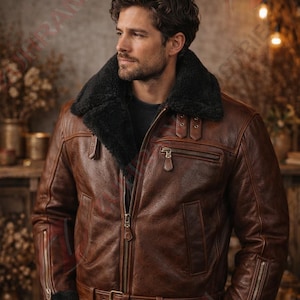 Puede incluir: Chaqueta de cuero marrón con cuello de borrego negro. La chaqueta tiene cierre de cremallera, múltiples bolsillos y cinturón en la cintura. Estilo clásico de bombardero.