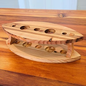 Puede incluir: Un expositor de madera artesanal con múltiples aberturas circulares. El expositor está hecho de madera de color claro y presenta un diseño curvo único. El expositor está diseñado para contener varios artículos. El expositor está sobre una superficie de madera.