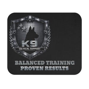 Puede incluir: Una alfombrilla de ratón rectangular negra con un emblema de escudo plateado metálico que incluye una calavera, tres estrellas y la silueta de un perro. El texto dice K9 TACTICAL SUPPORT, BALANCED TRAINING y PROVEN RESULTS en color plata.