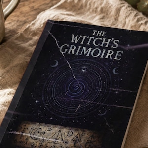 May include: A book titled The Witch's Grimoire with a dark cover featuring a celestial spiral design, an eye, and crescent moons. The lower section displays a rectangular panel filled with various occult symbols and geometric line drawings.