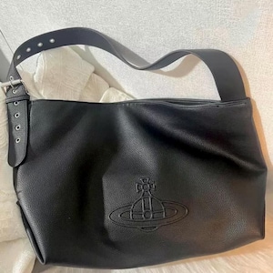 May include: Black leather shoulder bag with a large strap and a silver buckle. The bag features a debossed emblem on the front. The bag has a soft, textured appearance and a long, adjustable strap.
