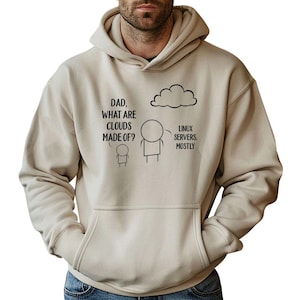Op de afbeelding: Een beige hoodie met een voorzak en een capuchon met trekkoord. De hoodie heeft een zwarte afbeelding met de tekst "DAD, WHAT ARE CLOUDS MADE OF?" en het antwoord "LINUX SERVERS, MOSTLY" met illustraties van stokfiguren.