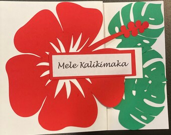 May include: A handmade greeting card featuring a large red hibiscus flower and green monstera leaves. The card includes the text "Mele Kalikimaka" in a white rectangle, perfect for a Hawaiian Christmas celebration.