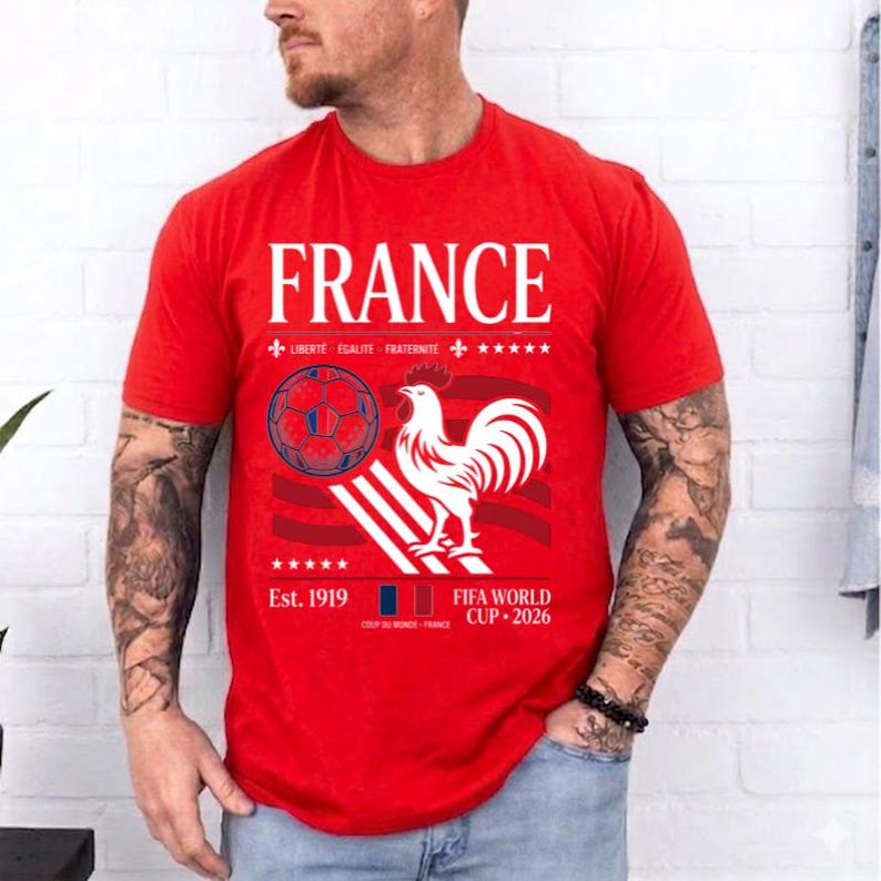 May include: A red short-sleeved t-shirt featuring the word FRANCE in white text, a graphic of a soccer ball, a white rooster, and the text LIBERTE EGALITE FRATERNITE, Est. 1919, and FIFA WORLD CUP 2026 printed in white on the front chest area.