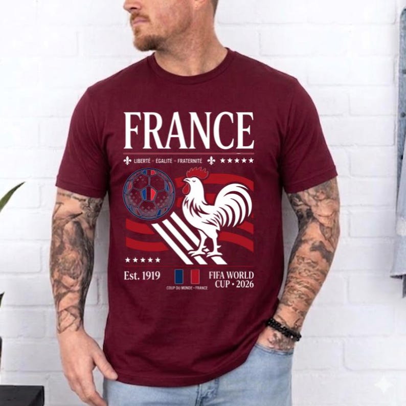 May include: A maroon short-sleeve t-shirt featuring the text FRANCE, a graphic of a soccer ball, a white rooster, and the text LIBERTE EGALITE FRATERNITE, Est. 1919, and FIFA WORLD CUP 2026. The design includes red and white stripes and five stars.