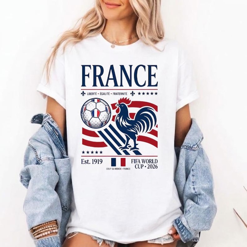 May include: A white short-sleeve t-shirt featuring a graphic with the text FRANCE, a soccer ball, a rooster, and the text FIFA WORLD CUP 2026. The design includes red, white, and blue stripes, the French flag, and the motto LIBERT&Eacute; &Eacute;GALIT&Eacute; FRATERNIT&Eacute;.