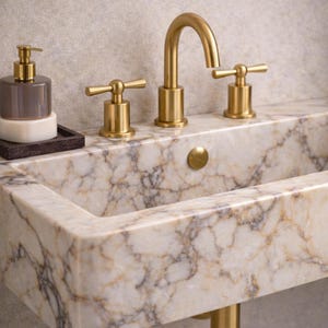 May include: A luxurious bathroom sink with a marble countertop and gold fixtures. The sink has a rectangular basin and a gold faucet with cross-shaped handles. A matching soap dispenser and tray are on the left.