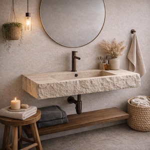 May include: A modern bathroom with a stone-like rectangular sink, dark bronze faucet, and a round mirror. A wooden shelf holds towels, and a small stool with a candle and towels sits nearby. A hanging plant and a woven basket add to the decor.
