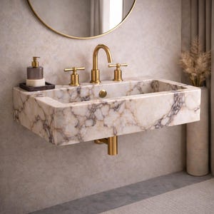 May include: A wall-mounted marble sink with gold fixtures. The sink has a rectangular basin with a veined pattern in shades of cream, brown, and gray. The gold faucet and handles complement the sink's design. A soap dispenser and mirror are also visible.
