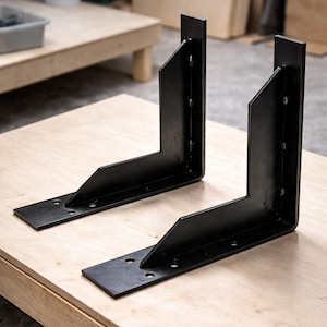 May include: Two black metal corner brackets with multiple pre-drilled holes, resting on a light-colored wooden surface. The brackets are L-shaped, designed for structural support in woodworking or construction projects.