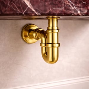 May include: A gold-colored plumbing fixture, likely a P-trap, is mounted on a light-colored wall. The fixture has a curved design with multiple connecting pieces. The top of the fixture is connected to a dark, patterned surface, possibly a countertop.