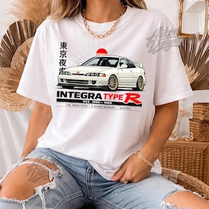 Könnte beinhalten: Weißes T-Shirt mit einem Autodesign. Das Design zeigt einen weißen Integra Type R mit goldenen Felgen, einer roten Sonne und japanischem Text. Der Text "INTEGRA TYPE R" wird angezeigt. Zusätzlicher Text enthält "DC2 1996-1998" und "1.8L DOHC VTEC / 5 SPEED MANUAL / 200 PS".